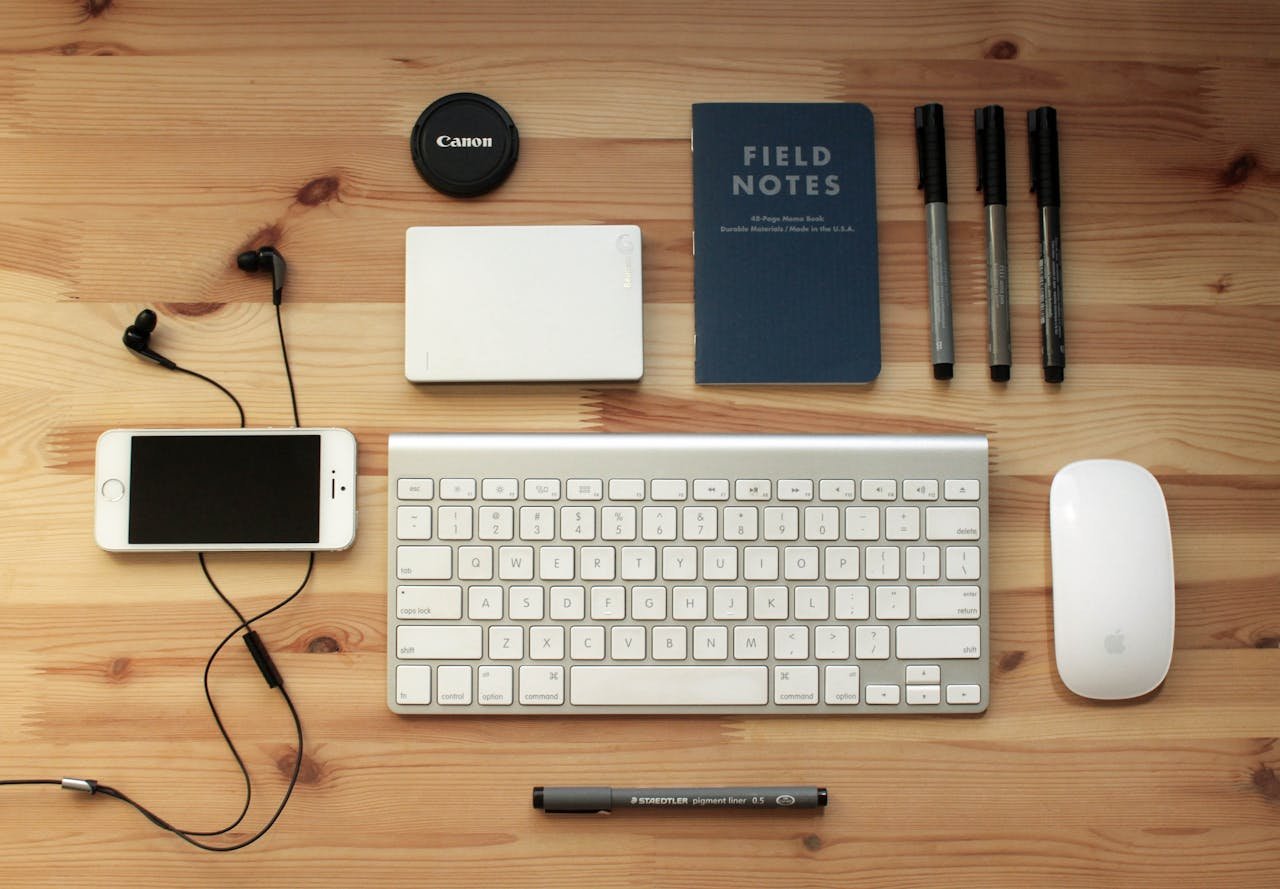 Services Top view of a modern desk setup featuring electronics, stationery, and gadgets on a wooden surface.